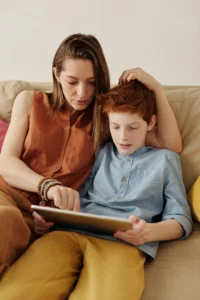 A women and pre-teen sitting on a couch, interacting with a tablet computer.