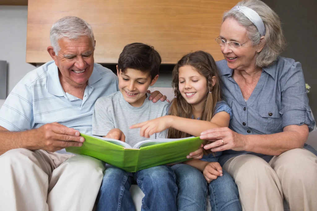 Grandparents sitting on a couch with two grandkids between them, interacting with a book.