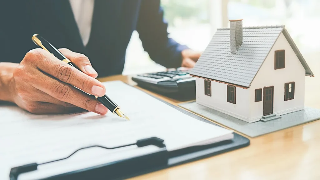 An attorney working at a desk with a contract, miniature house and calculator.