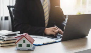 An attorney typing at the computer with a small house on the desk.