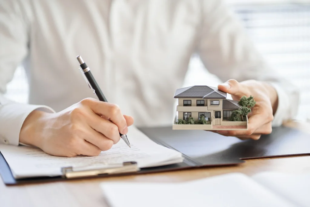 A woman writing a contract, holding a miniature house.