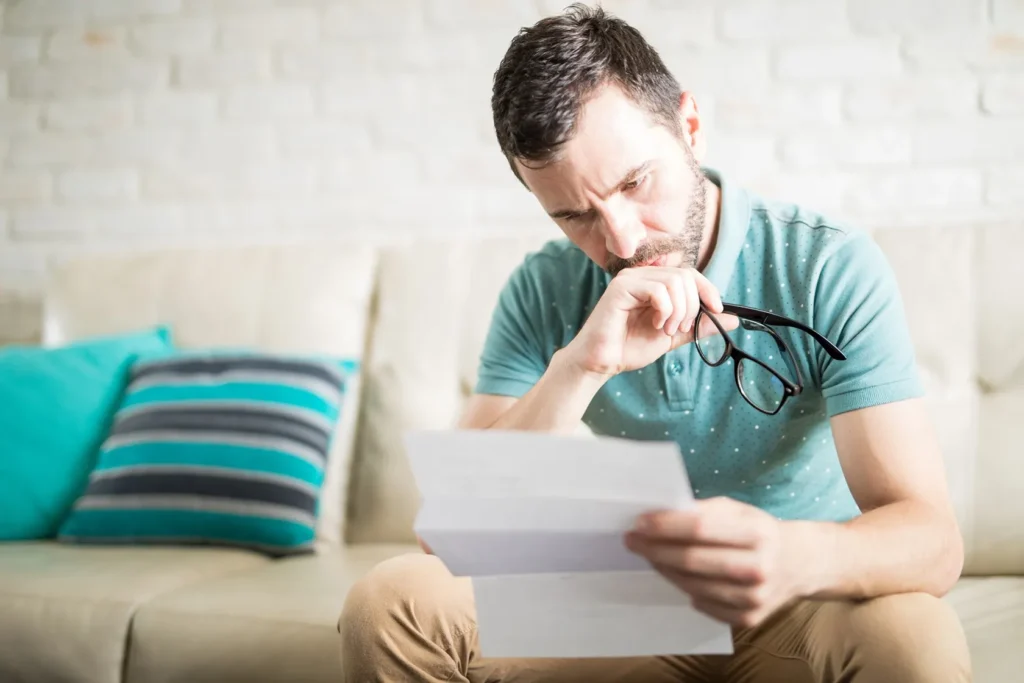 Man sitting on a couch, looking at a document nervously.