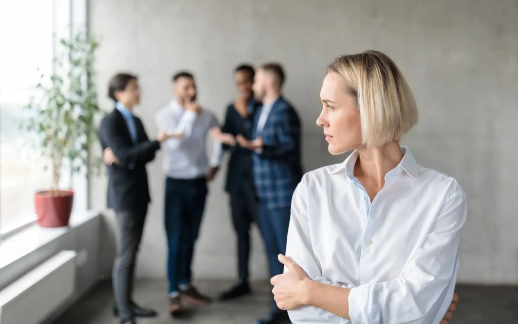 A group of people engaged in conversation and a women standing off to the side, not engaged.